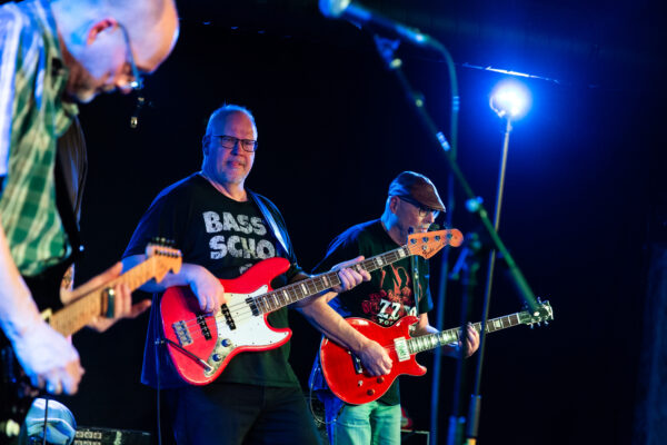 Im Vordergrund spielt der Gitarrist hoch konzentriert, während der Bassist sich auf die Zunge beisst bei einem ganz besonders aufwendigem Riff.