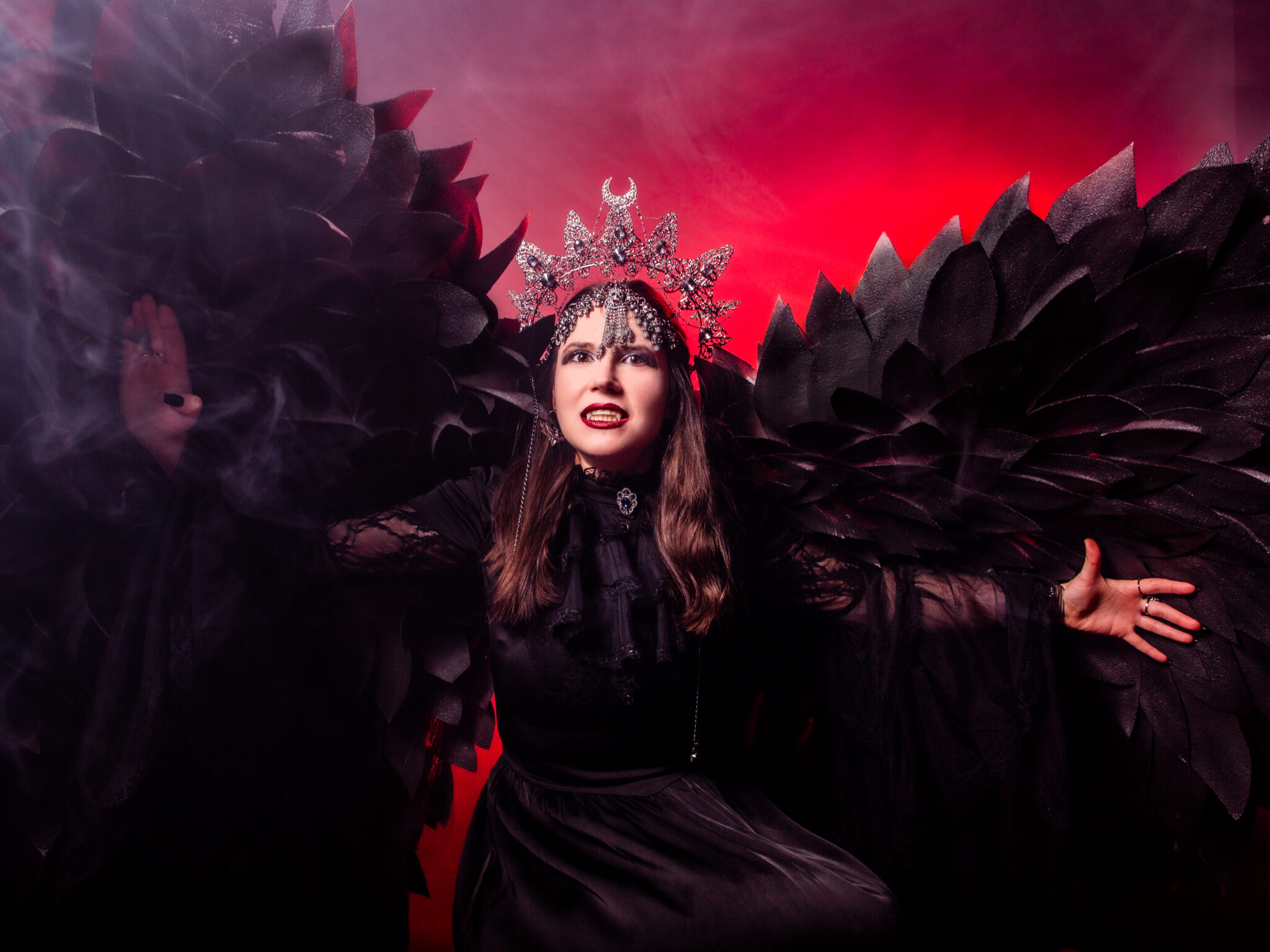 Episches künstlerisches Portrait einer Frau mit großen schwarzen Flügeln und Krone, inszenierte Bildserie mit rotem Licht und Nebel, fotografiert von einer Fotografin in Bremen